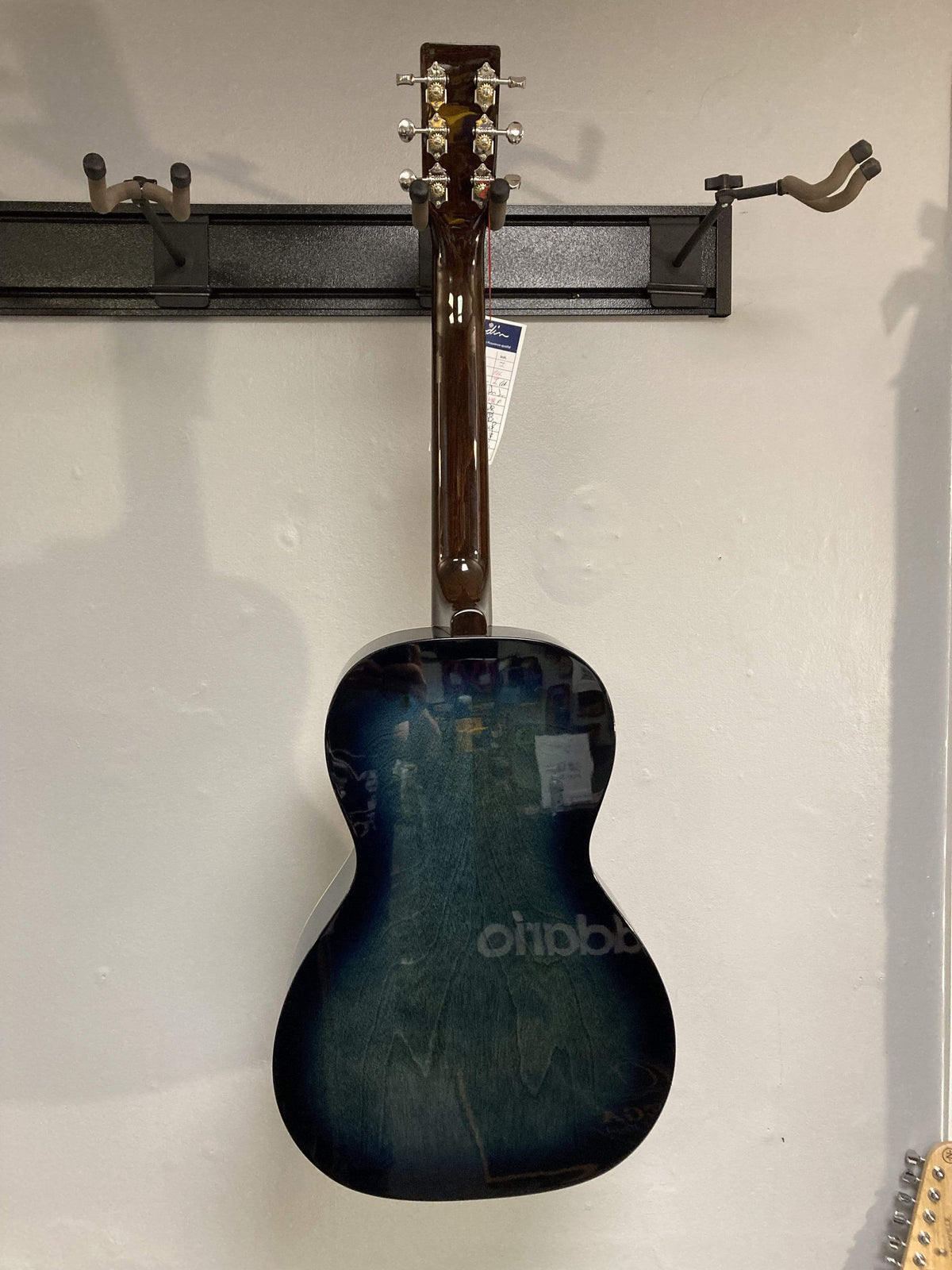 Rear view of the Art & Lutherie Roadhouse HG Indigo Burst Q-Discrete parlor guitar, featuring a solid spruce top, hanging on a wall rack with a price tag on the headstock.