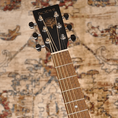A close-up of the Bodhi BG10E Spruce Top Concert Body Acoustic-Electric Guitar's headstock and fretboard highlights its tuning pegs, with a patterned rug in the background. Ideal for fingerpicking guitar enthusiasts.