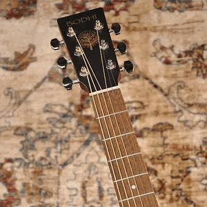 A close-up of the Bodhi BG10E Spruce Top Concert Body Acoustic-Electric Guitar's headstock and fretboard highlights its tuning pegs, with a patterned rug in the background. Ideal for fingerpicking guitar enthusiasts.