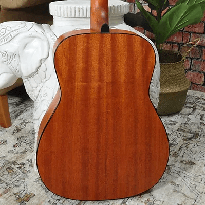 The back view of the Bodhi BG10E Spruce Top Concert Body Acoustic-Electric Guitar by Bodhi is shown resting on a patterned rug, with a white decorative piece and a potted plant in the background.