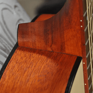 Close-up of the neck joint on the Bodhi BG10E Spruce Top Concert Body Acoustic-Electric Guitar, highlighting its mahogany grain, reddish-brown finish, and fretboard with metal frets and strings visible on the right.