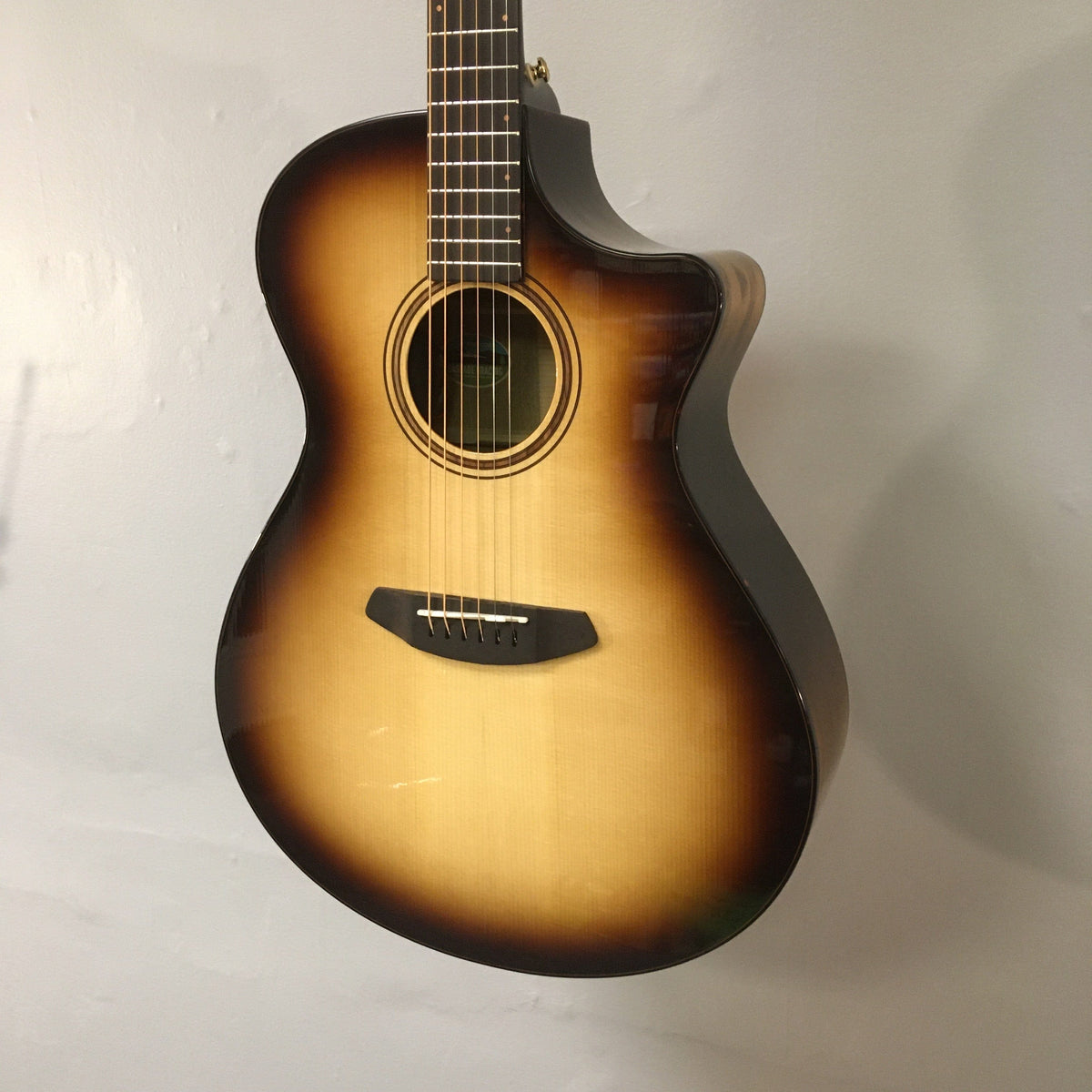 Breedlove Artista Pro Concerto Burnt Amber CE European-Myrtlewood guitar on a stand, showcasing its spruce top, myrtlewood back and sides, and detailed brass inlays.