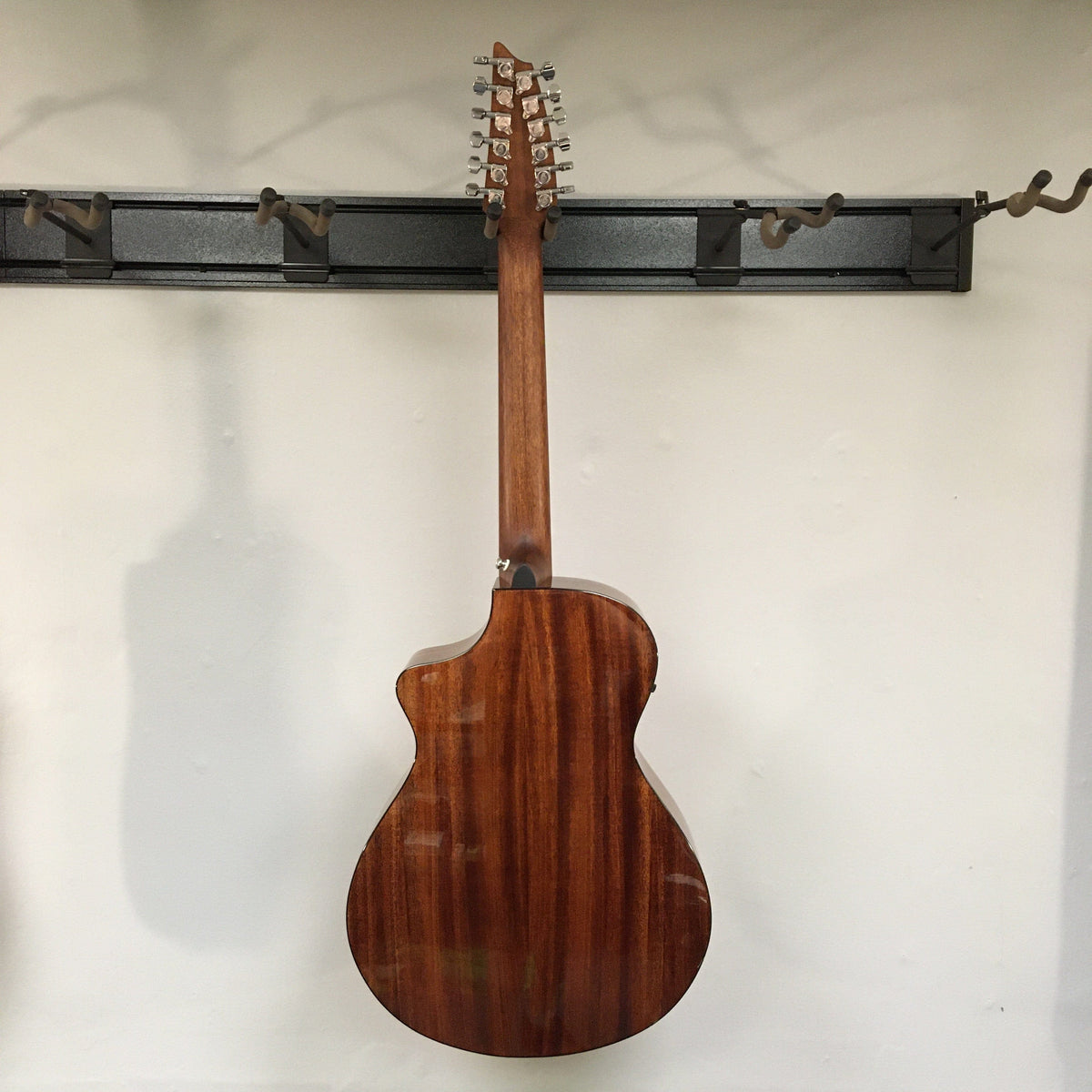 Breedlove Discovery S Concert CE 12-string Edgeburst guitar on a wall hook, showcasing its detailed craftsmanship and blemish.
