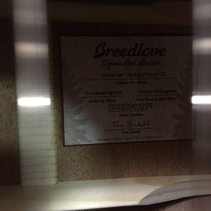 Breedlove Performer Pro Concert Aged Toner CE European-African Mahogany guitar with case, displayed on a wall with descriptive sign and specifications.
