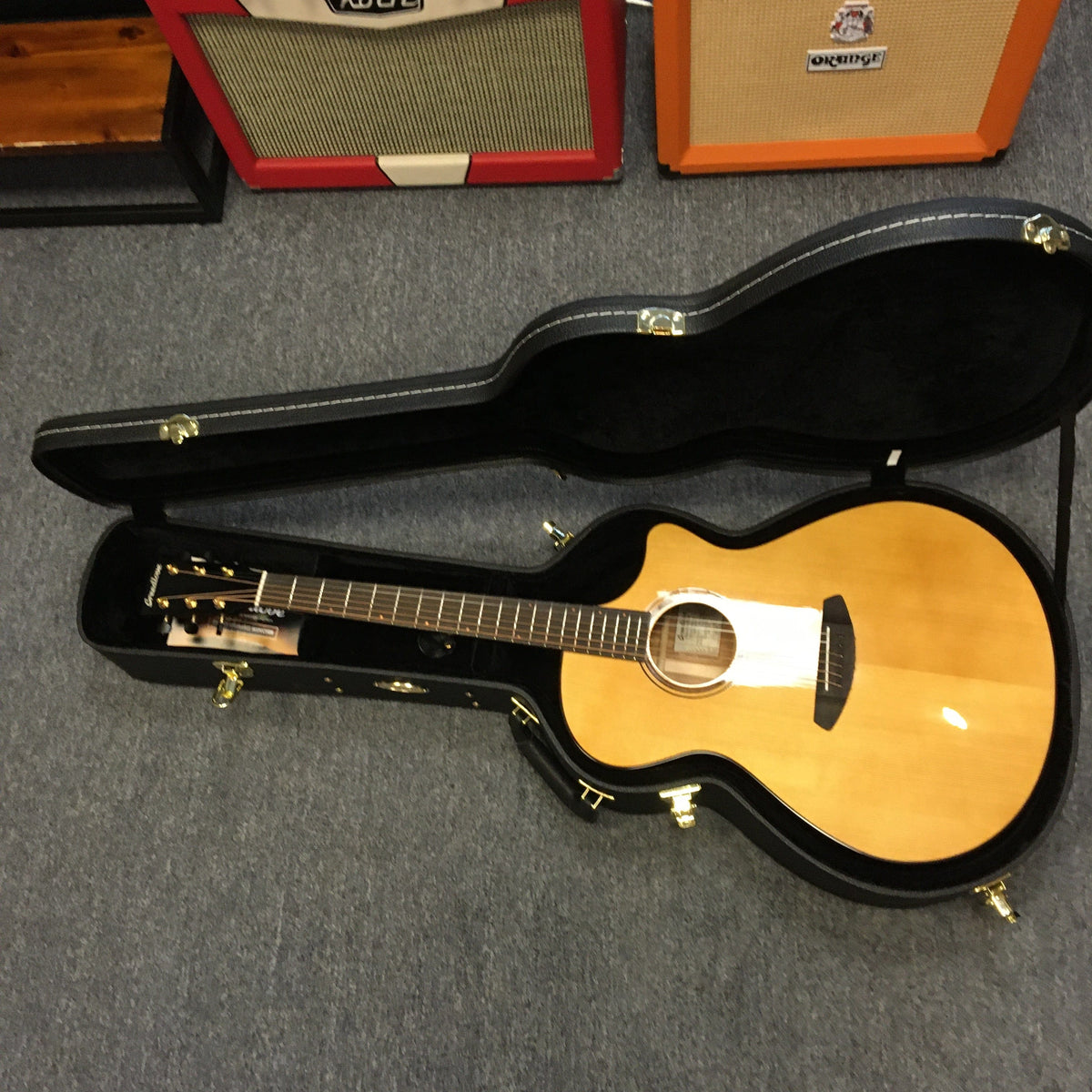 A Breedlove Performer Pro Concerto Aged Toner guitar is shown in an open Gator gigbag on a carpeted floor, with amplifiers in the background, emphasizing its premium acoustic quality.