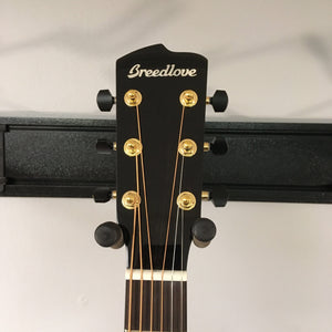 Close-up of the headstock of a Breedlove Performer Pro Concerto Aged Toner w/Gator Gigbag, featuring gold tuning pegs on a wall hanger against a light background, highlighting its signature refined acoustic tone.