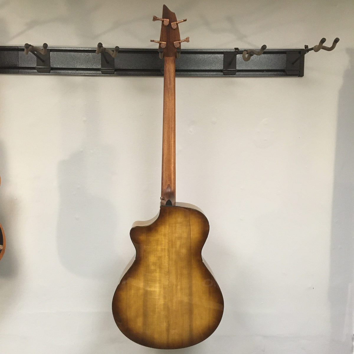 Breedlove Pursuit Exotic S Concerto Amber Bass CE B-Stock hanging on a wall hook, showcasing its myrtlewood body and mahogany neck.