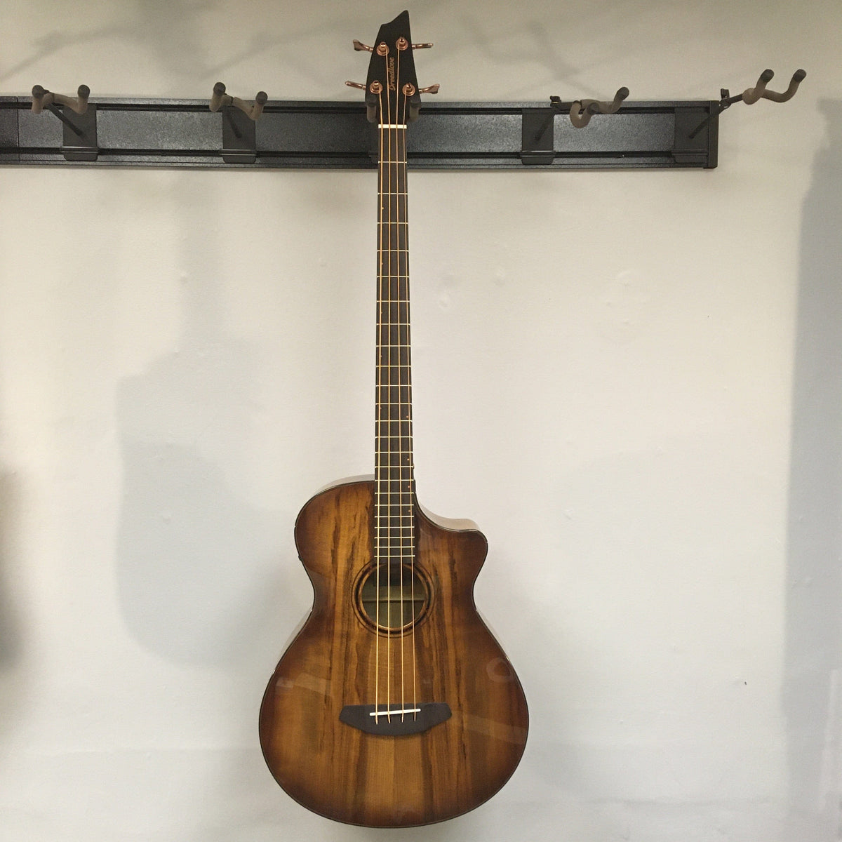 Breedlove Pursuit Exotic S Concerto Amber Bass CE B-Stock hanging on wall, showing close-up details of strings and body finish blemishes.