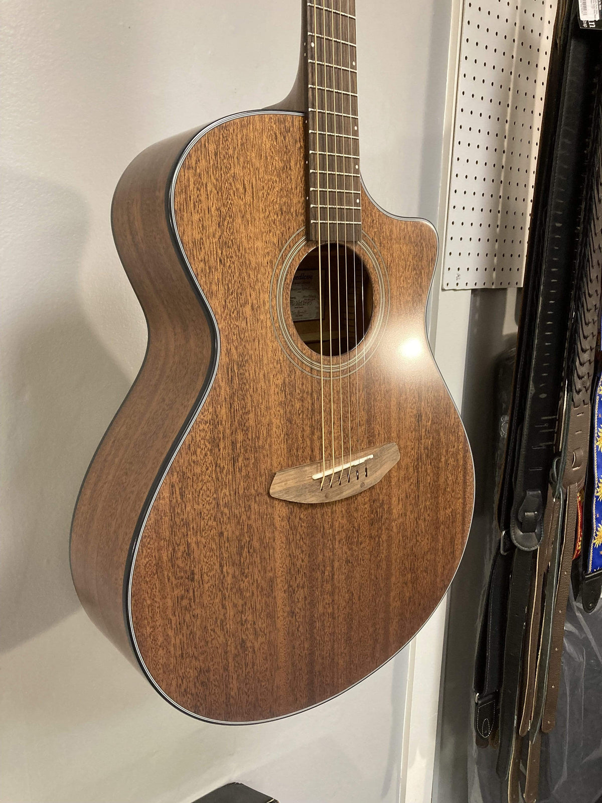 Breedlove Wildwood Concerto Satin CE Solid African Mahogany guitar displayed on a wall.