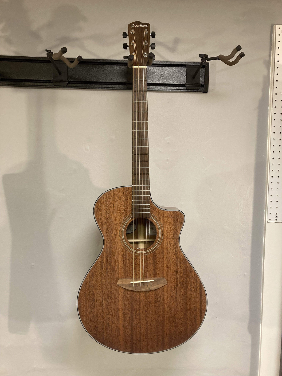 Breedlove Wildwood Concerto Satin CE Solid African Mahogany guitar mounted on a wall, showcasing its elegant body and craftsmanship.
