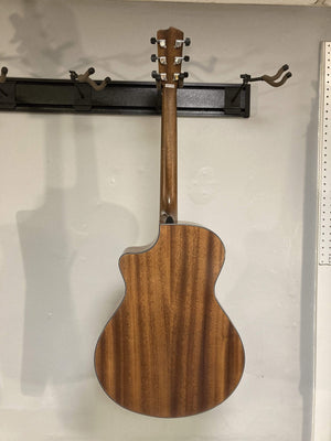 Breedlove Wildwood Concerto Satin CE Solid African Mahogany guitar displayed on a wall, highlighting its sleek design and premium wood craftsmanship.