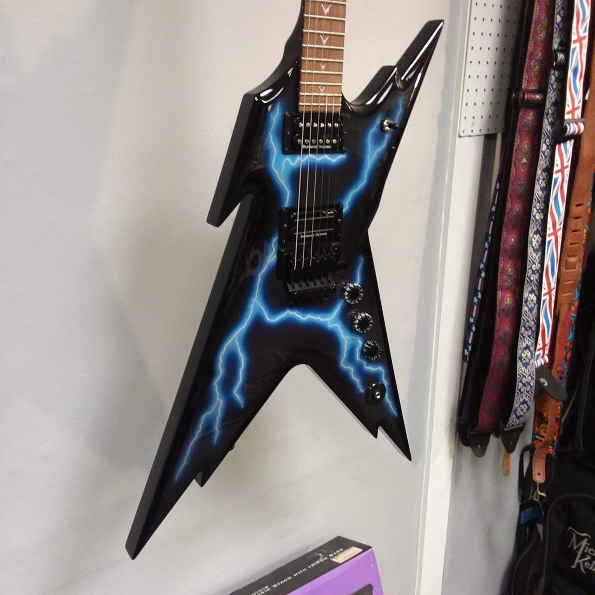 Dean Razorback Lightning B Stock electric guitar on a wall, featuring a lightning graphic and close-up of strings and headstock.