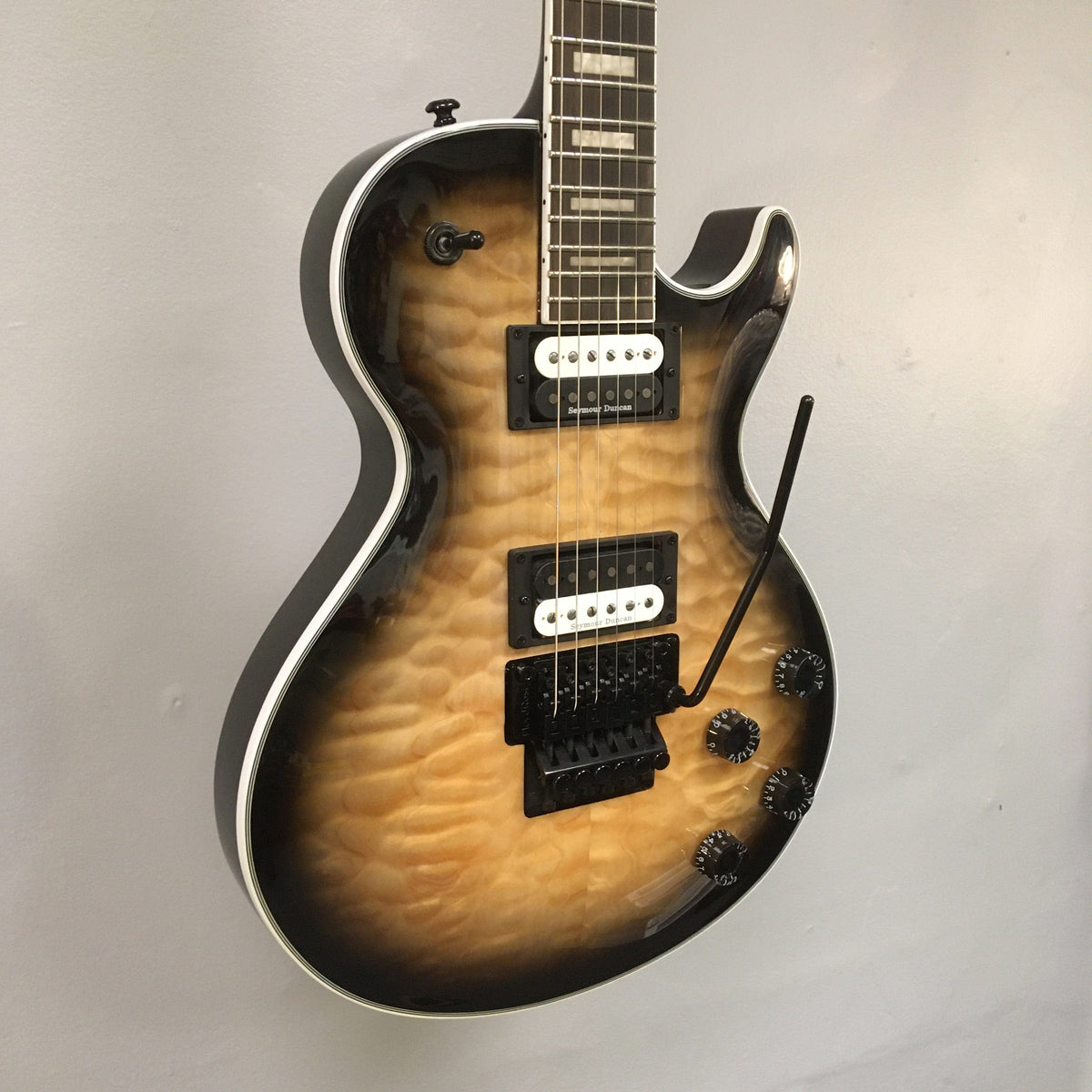 Dean Thoroughbred Select Quilt-top guitar with Floyd Rose bridge, displayed on a wall, showcasing its detailed craftsmanship and professional features.