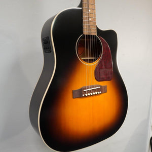 Epiphone Masterbilt J-45 EC Aged Vintage Sunburst Gloss guitar displayed on a wall, showcasing its sloped shoulder body and solid Sitka spruce top.
