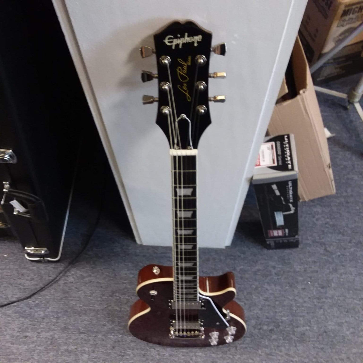 Epiphone Les Paul Modern guitar leaning against a wall, showcasing its sleek design and modern features like slim taper neck and contoured heel.