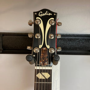 Godin 5th Avenue Jumbo P90 Harvest Gold guitar on a stand with visible fret markers, redesigned headstock, and Godin logo.