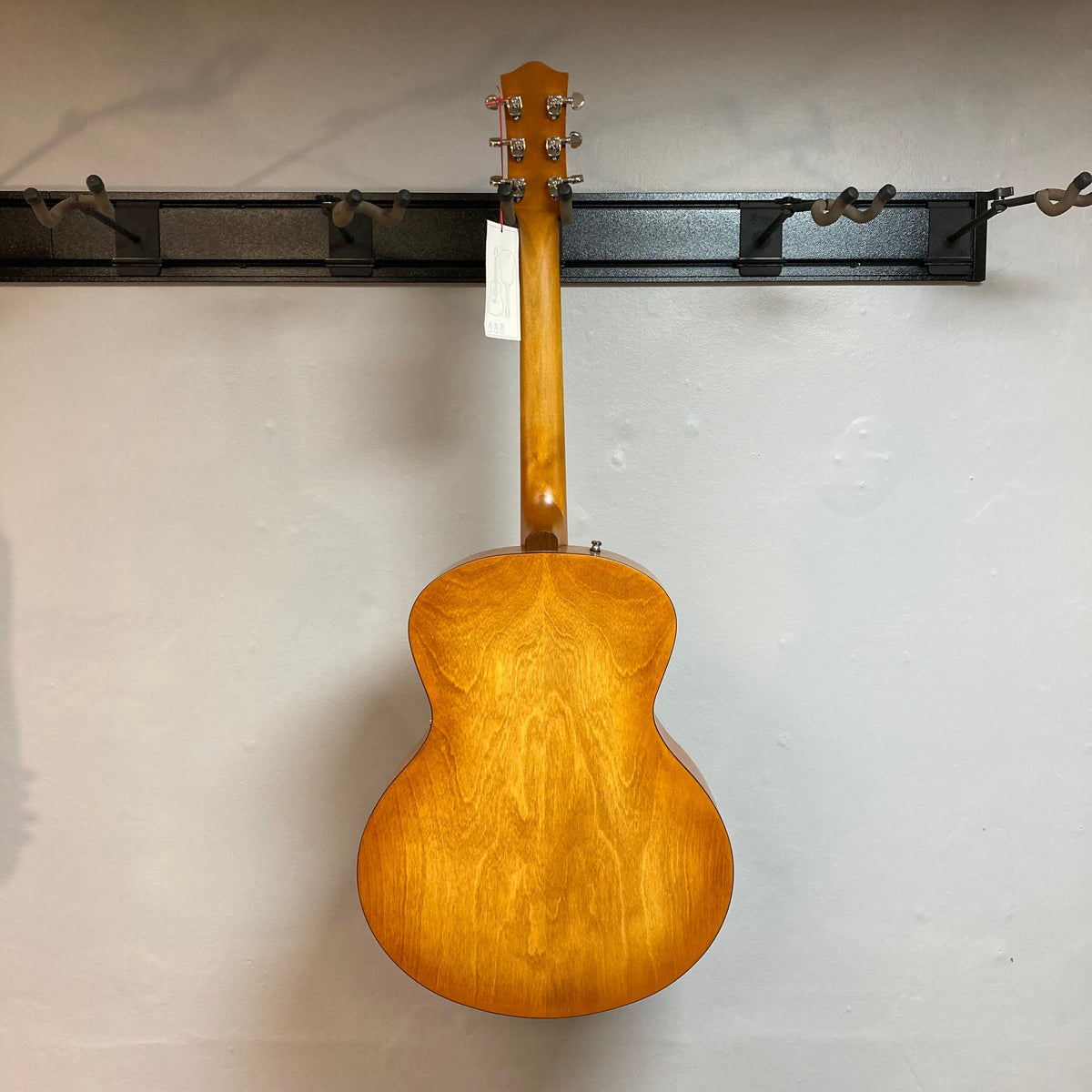 Godin 5th Avenue Jumbo P90 Harvest Gold guitar mounted on a wall, featuring a redesigned headstock and large fret markers.