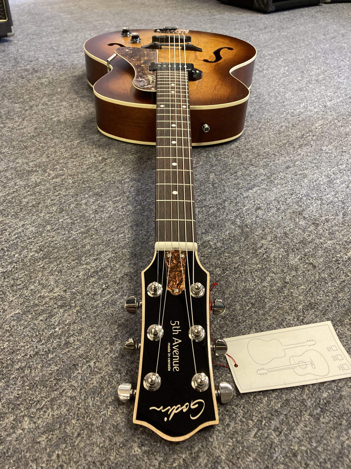 Godin 5th Avenue Kingpin P90 Cognac Burst electric guitar with arched top, floating pickguard, and high-gloss headstock lying on the floor.