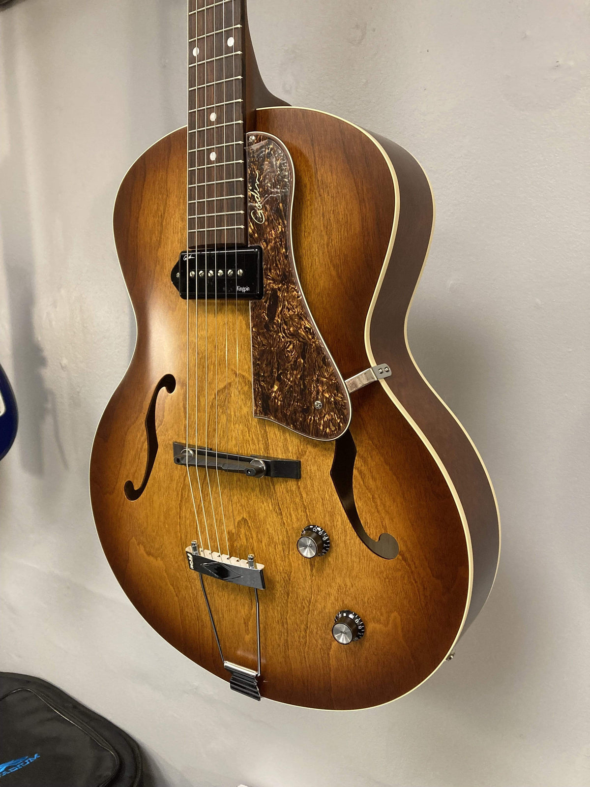 Godin 5th Avenue Kingpin P90 Cognac Burst archtop guitar on a stand, featuring a floating pickguard and high-gloss headstock.