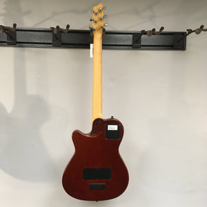 Godin A6 Ultra Baritone Burnt Umber guitar hanging on a wall, showcasing its chambered body and custom mini-humbucker pickup.