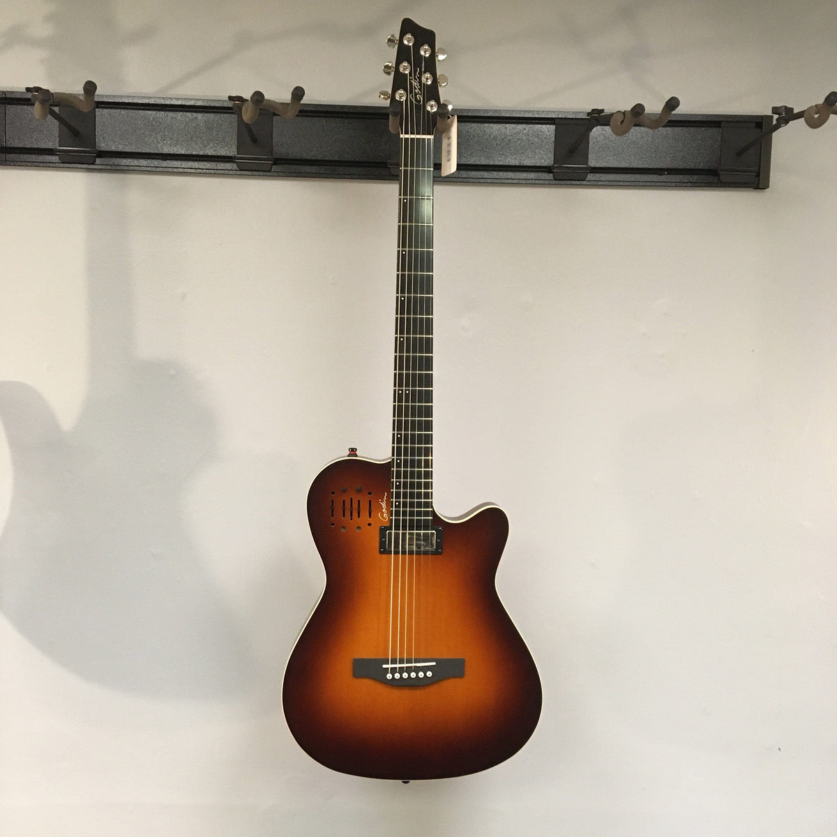 Godin A6 Ultra Baritone guitar with mini-humbucker, acoustic transducer, and dual outputs, displayed against a white wall.