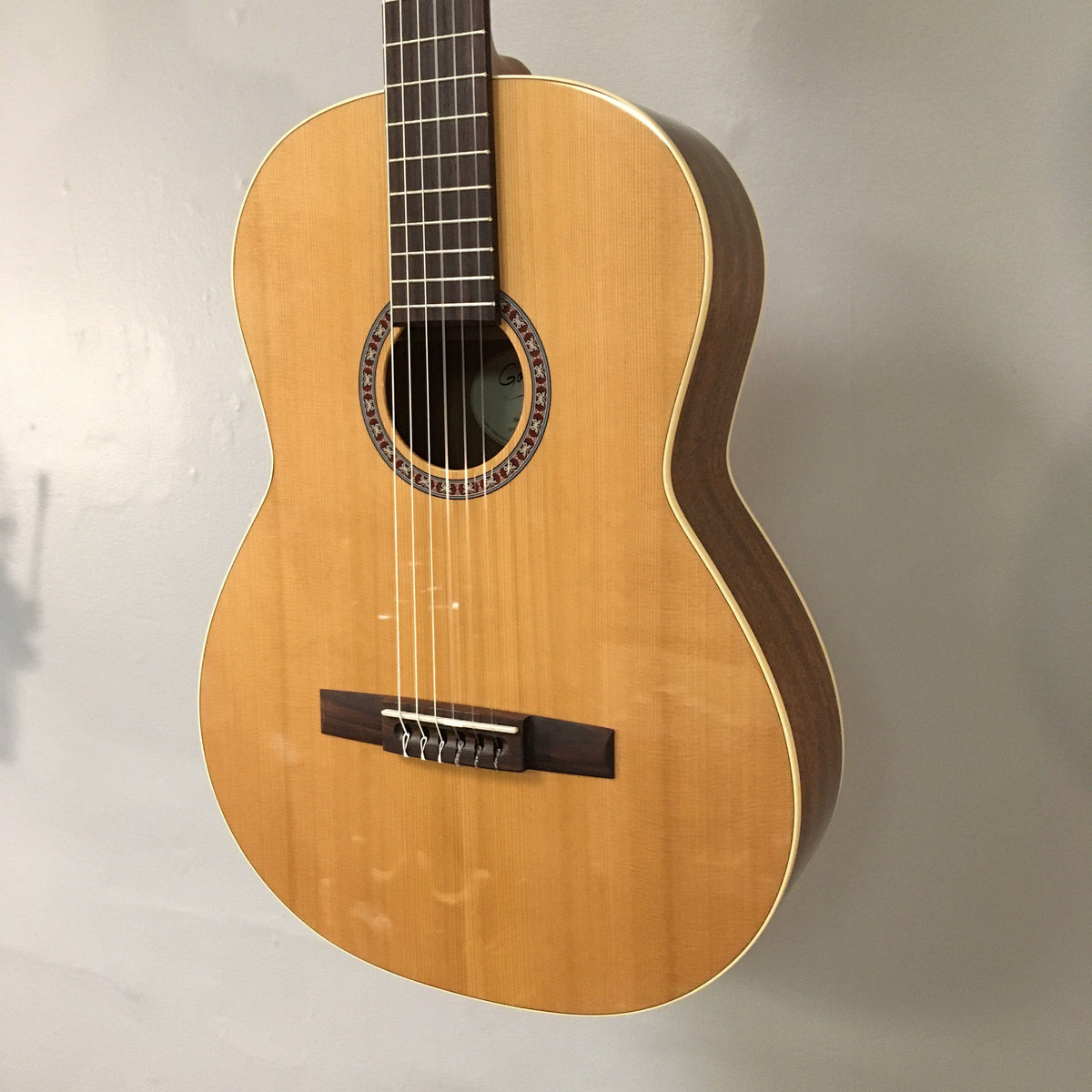 Godin Concert Nylon String Classical Guitar, featuring a high gloss finish, solid mahogany body, and solid cedar top, shown mounted on a wall.