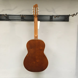 Godin Etude Classical Guitar, full-size, on a hook with a tag, showcasing its solid cedar top and Canadian wild cherry back.