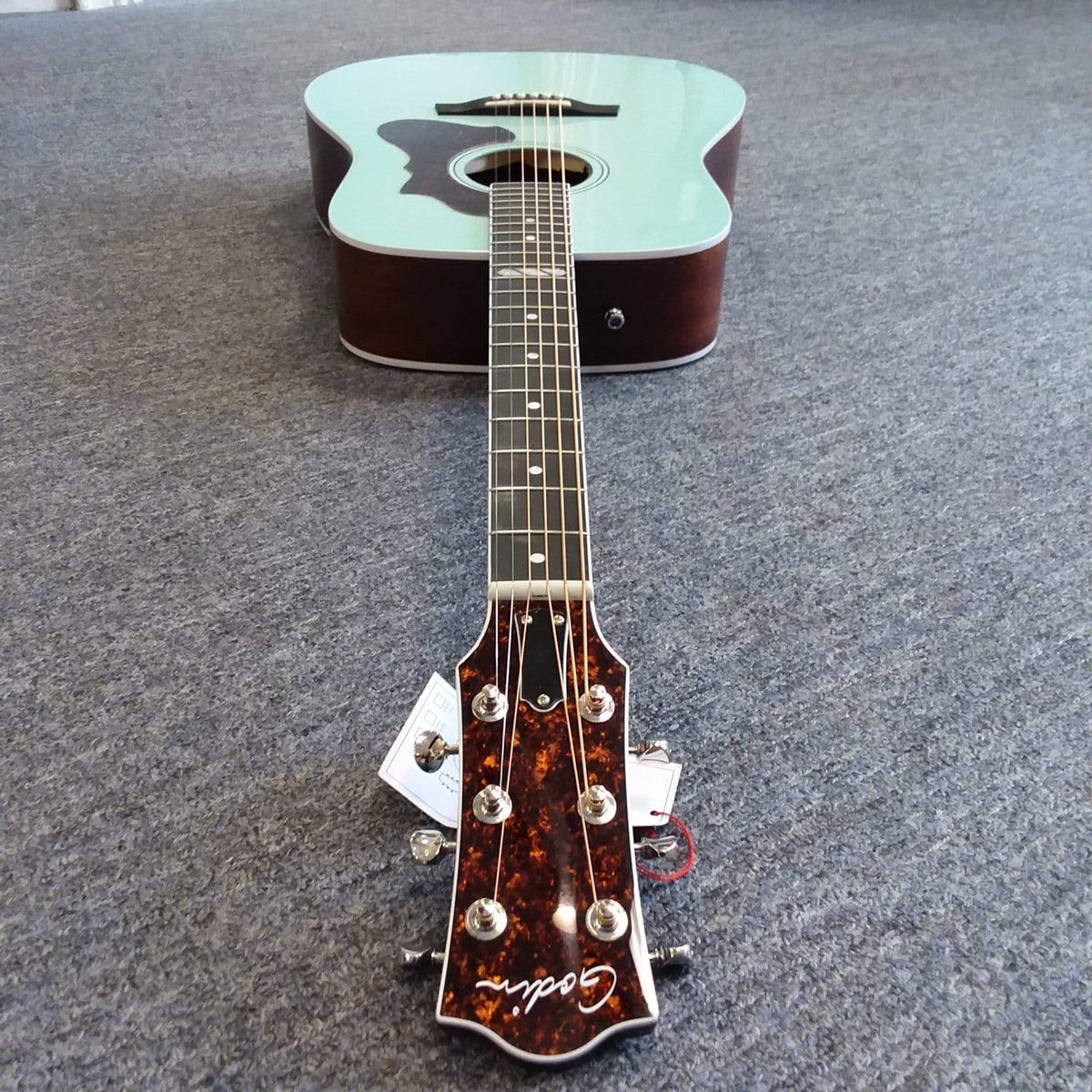 Godin Imperial Laguna Blue GT EQ acoustic guitar with solid mahogany back, Sitka spruce top, and LR Baggs Anthem system, lying on the floor.