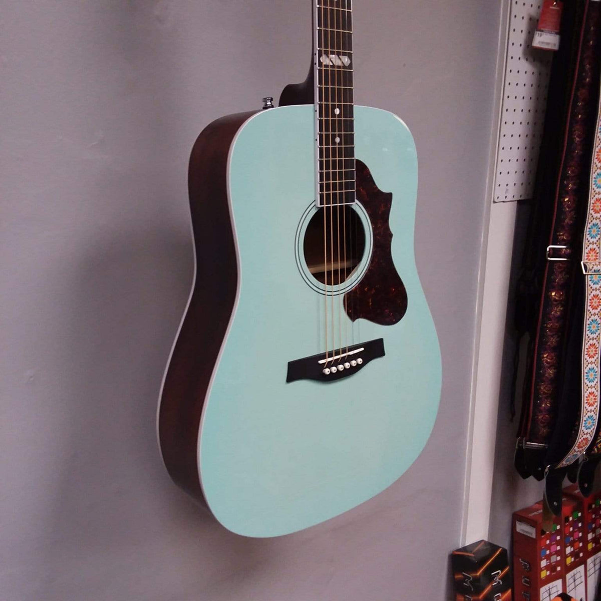 Godin Imperial Laguna Blue GT EQ acoustic guitar with mahogany back, spruce top, and onboard preamp, displayed on a wall.