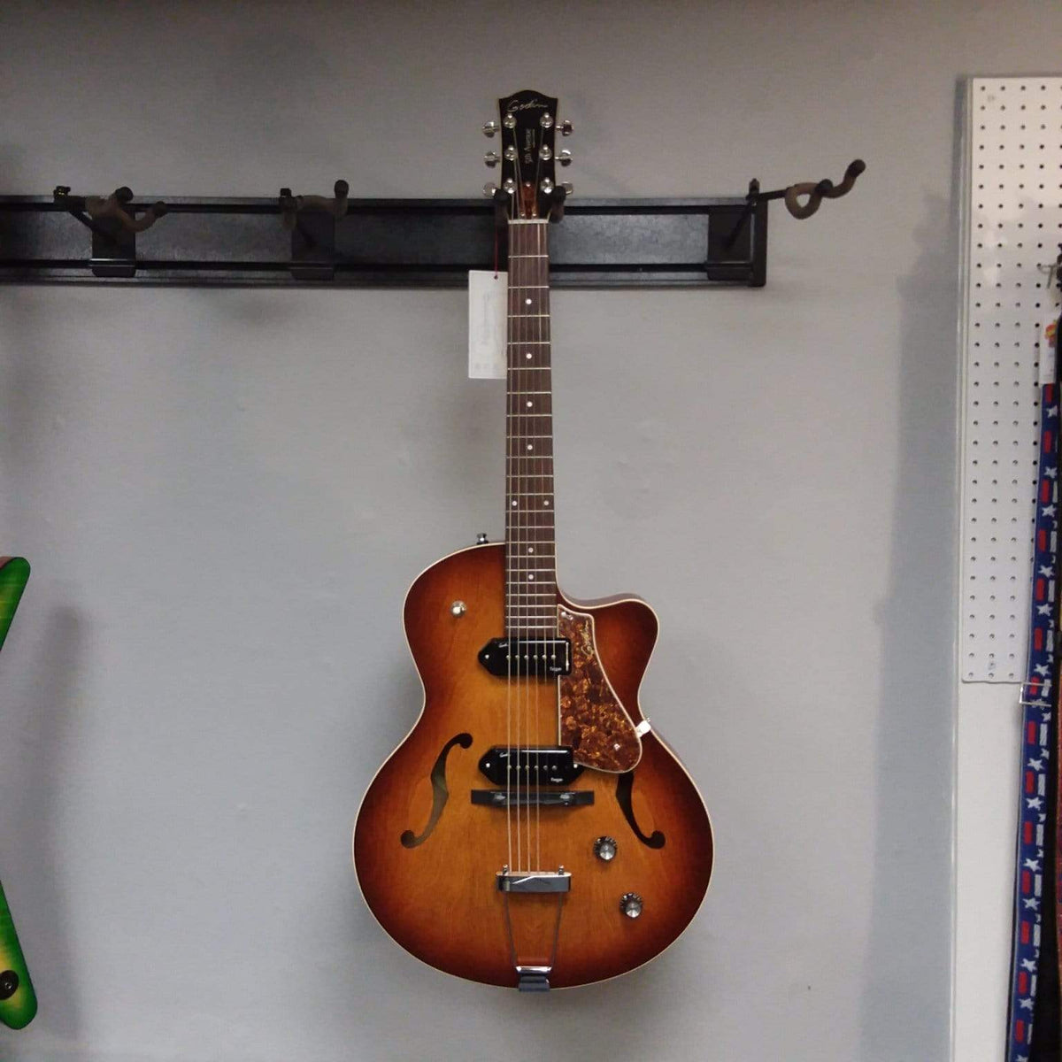 Godin 5th Avenue CW Kingpin II Cognac Burst guitar with P90 pickups, displayed on a wall.