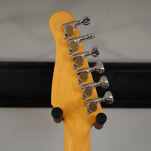 The back of a Godin RG3 Passion Lace Sensor Hot Gold Indigo Blue guitar headstock, featuring six chrome tuning pegs and a visible serial number, is shown resting on black stand arms against a neutral background.