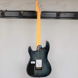 A Godin RG3 Passion Lace Sensor Hot Gold electric guitar in Indigo Blue with a gig bag is displayed on a wall rack, shown from the back. The light wood neck, tags, and barcode label are visible.