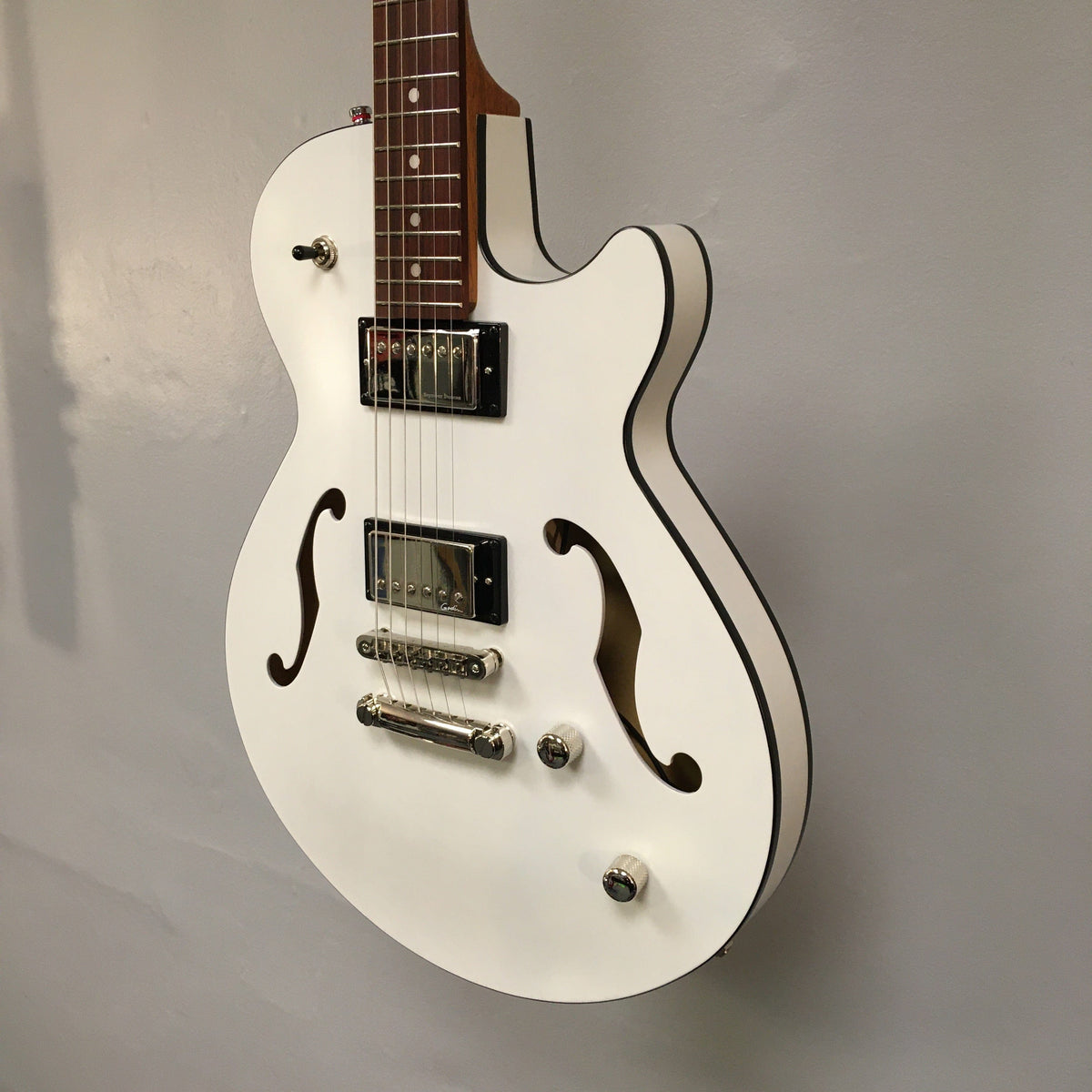 Godin Montreal Premiere HT Trans White electric guitar with black trim and visible strings, displayed against a wall.