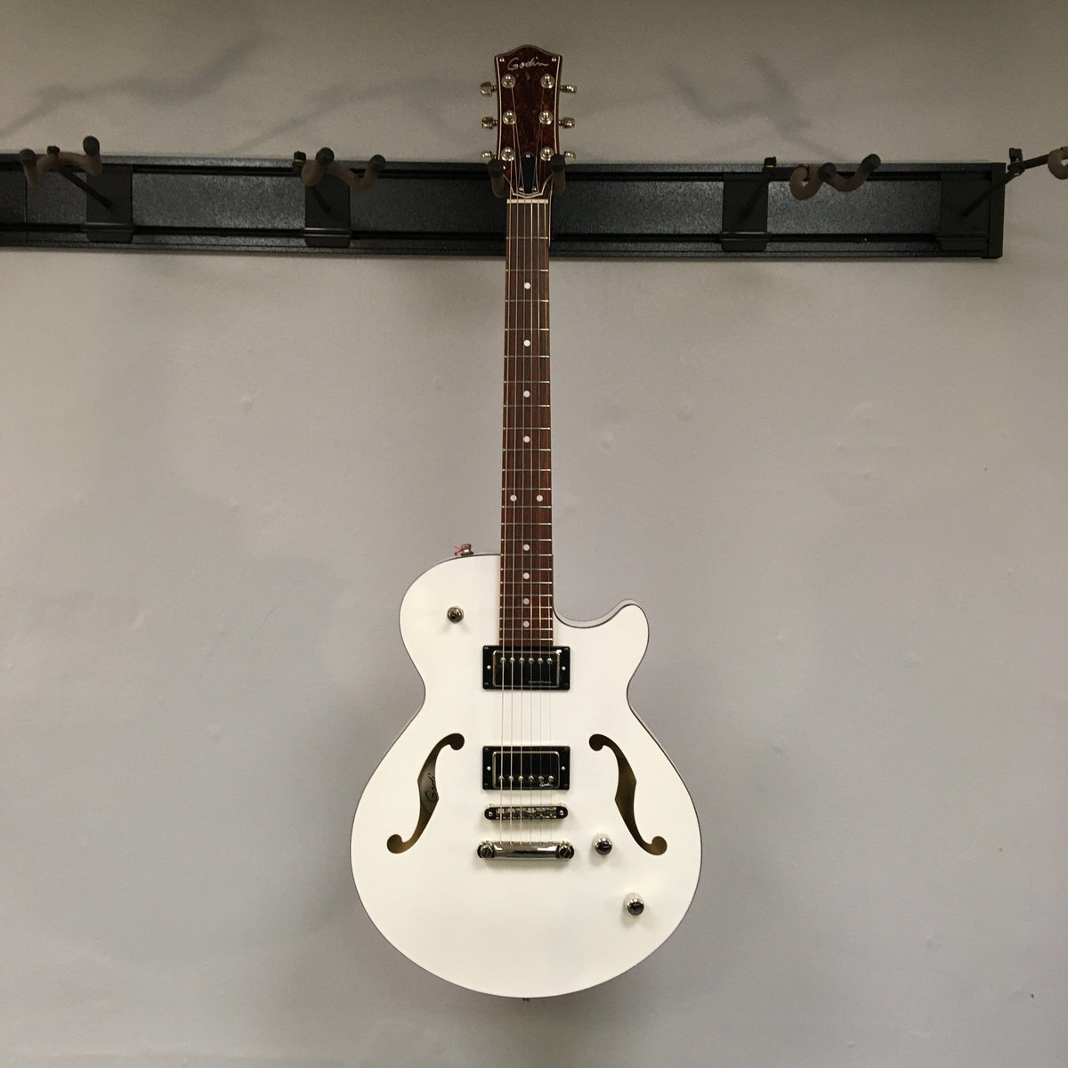Godin Montreal Premiere HT Trans White guitar on a wall, highlighting its elegant design and build.