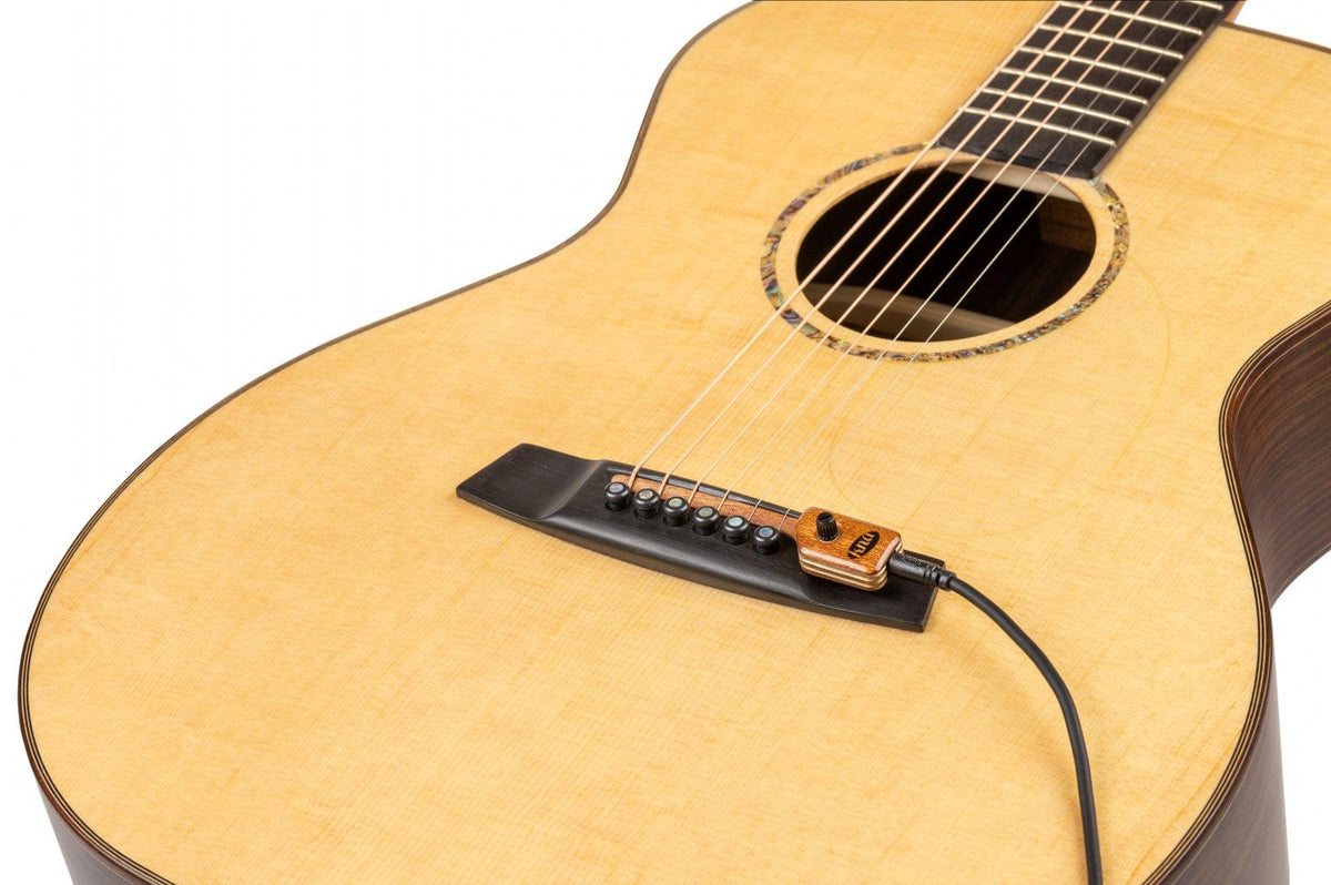 KNA SG-2 Portable Piezo Pickup for Steel String Guitar with Volume Control, shown close-up on an acoustic guitar's bridge, highlighting its integration without modifications.