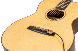 KNA SG-2 Portable Piezo Pickup for Steel String Guitar with Volume Control, shown close-up on an acoustic guitar's bridge, highlighting its integration without modifications.