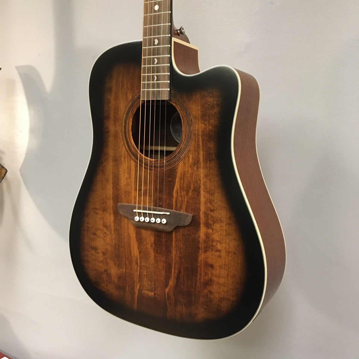 Luna Art Vintage Dreadnought Acoustic/Electric Guitar hanging on a wall, showcasing its brushed nickel tuners and solid spruce top.