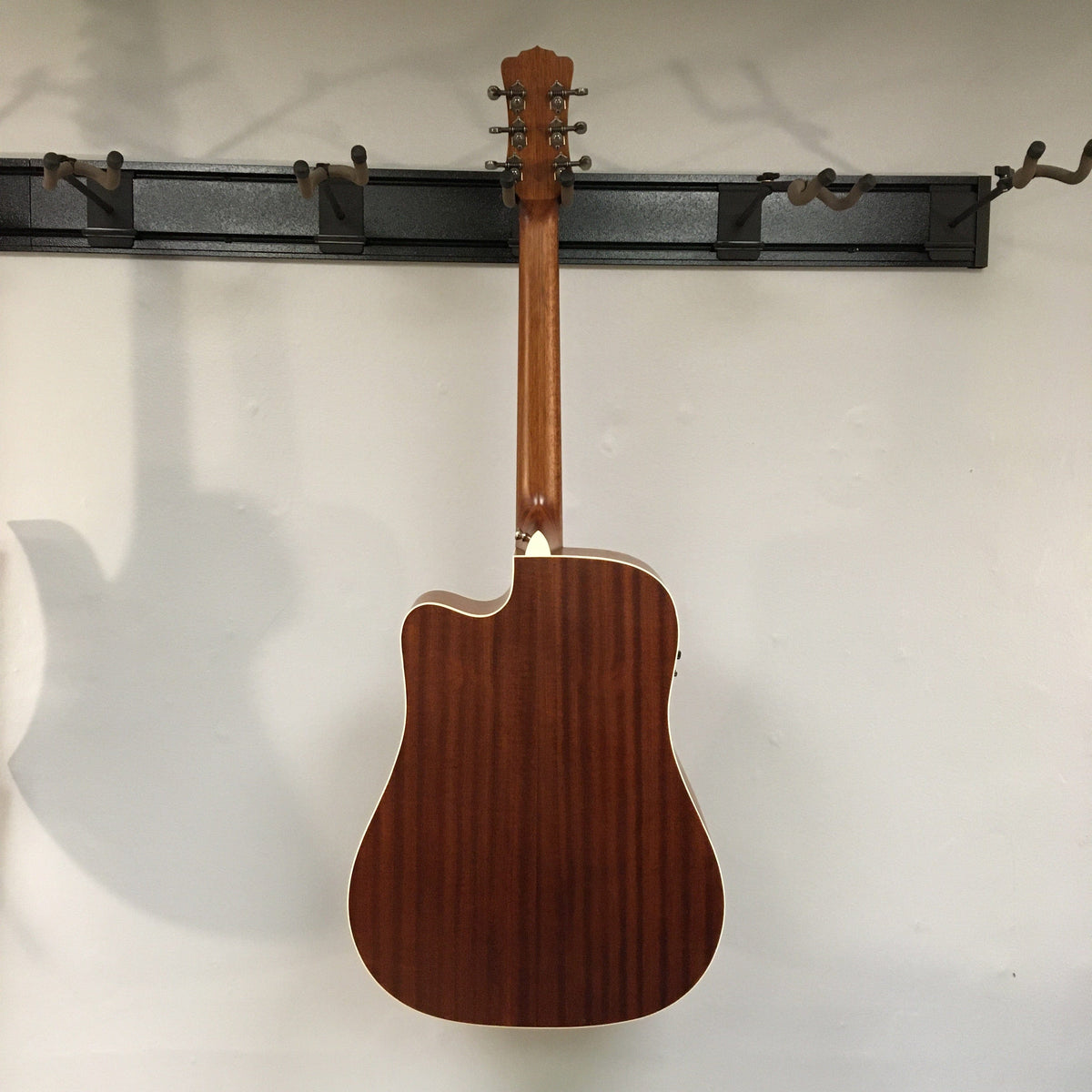 Luna Art Vintage Dreadnought Acoustic/Electric Guitar hanging on a wall, showcasing its rustic finish and solid-built construction.
