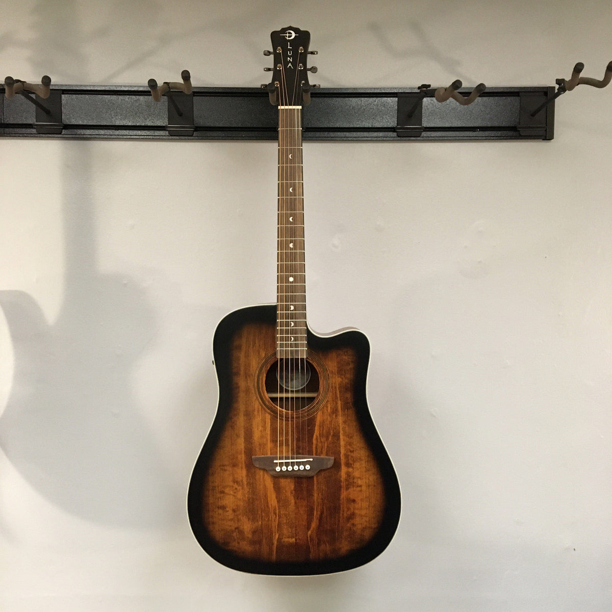 Luna Art Vintage Dreadnought Acoustic/Electric Guitar with moon phase inlays, distressed brownburst finish, and open gear tuners, displayed on a wall.