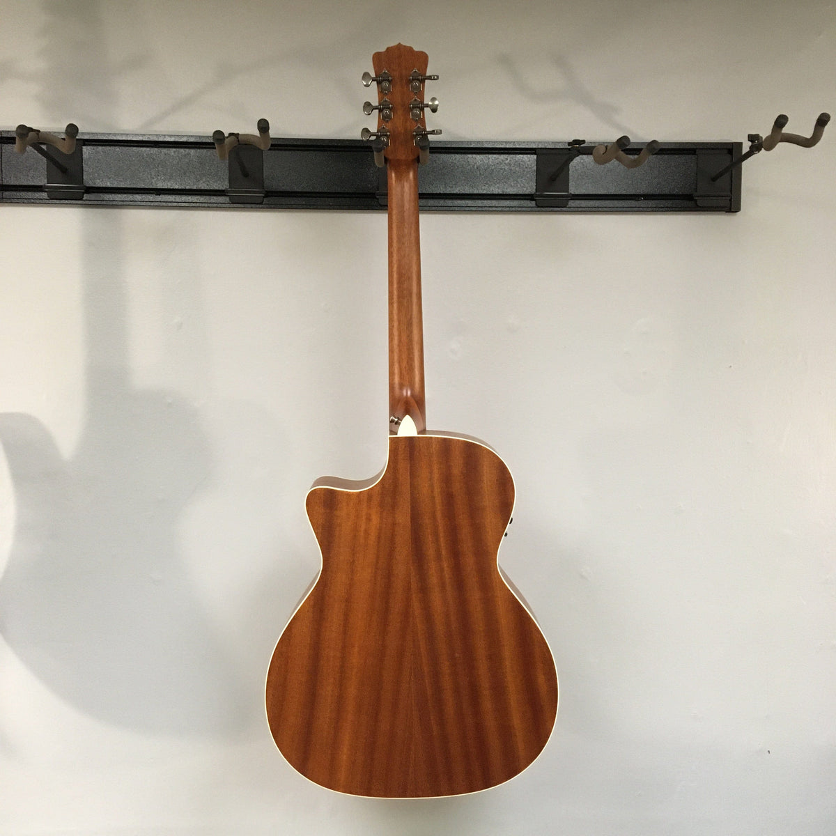 Luna Art Vintage Grand Auditorium Solid Top Cutaway A/E guitar mounted on a wall, showcasing its mahogany body, spruce top, and brushed nickel open gear tuners.