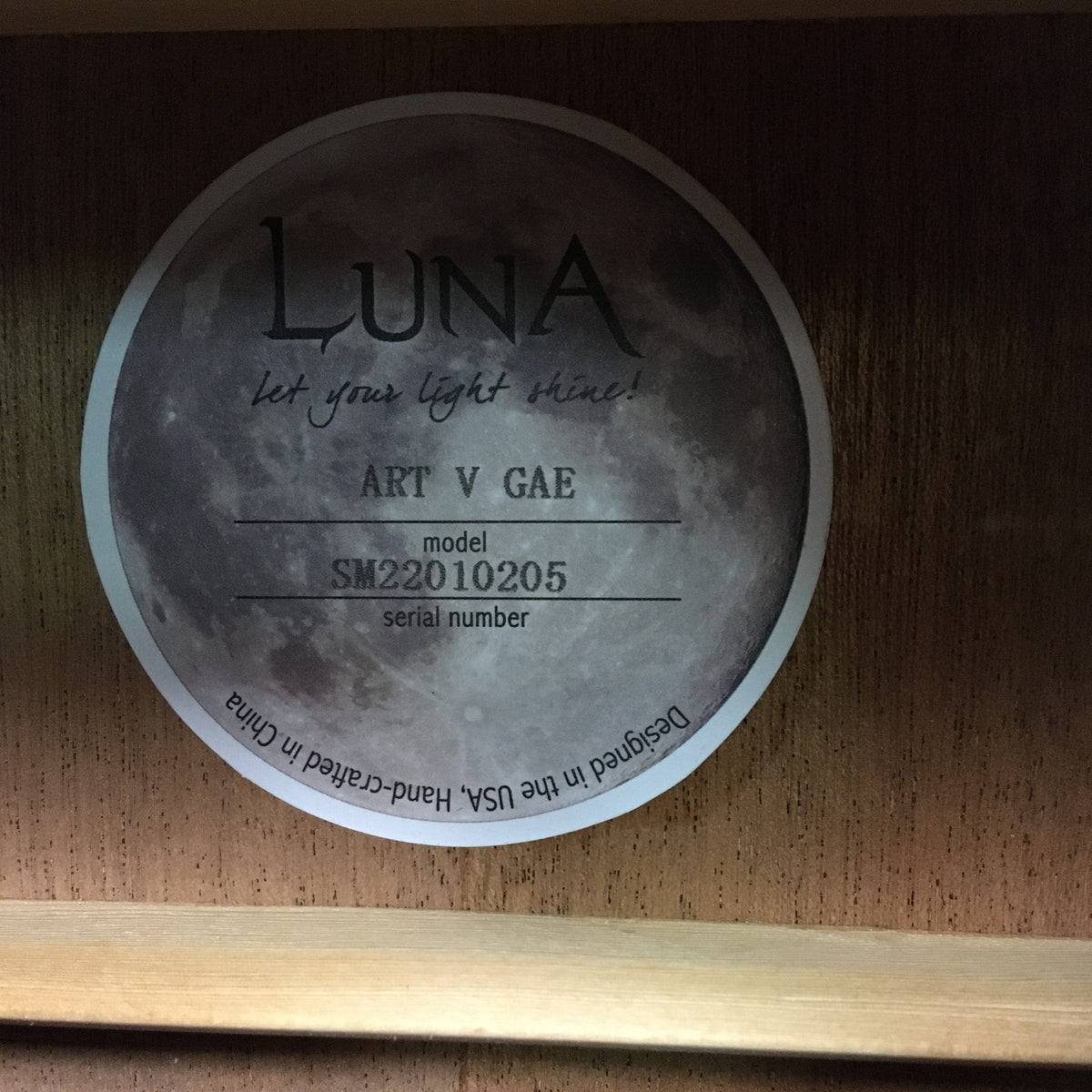 Luna Art Vintage Grand Auditorium guitar featuring a circular label on a wooden surface with brushed nickel tuners and vintage brown burst finish.