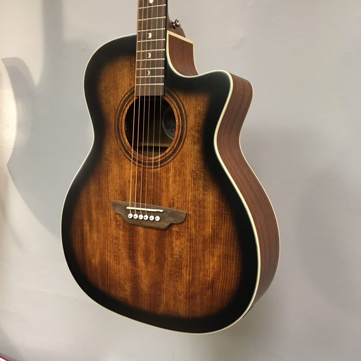 Luna Art Vintage Grand Auditorium Solid Top Cutaway A/E displayed on a wall, highlighting its vintage brown burst finish and open gear tuners.