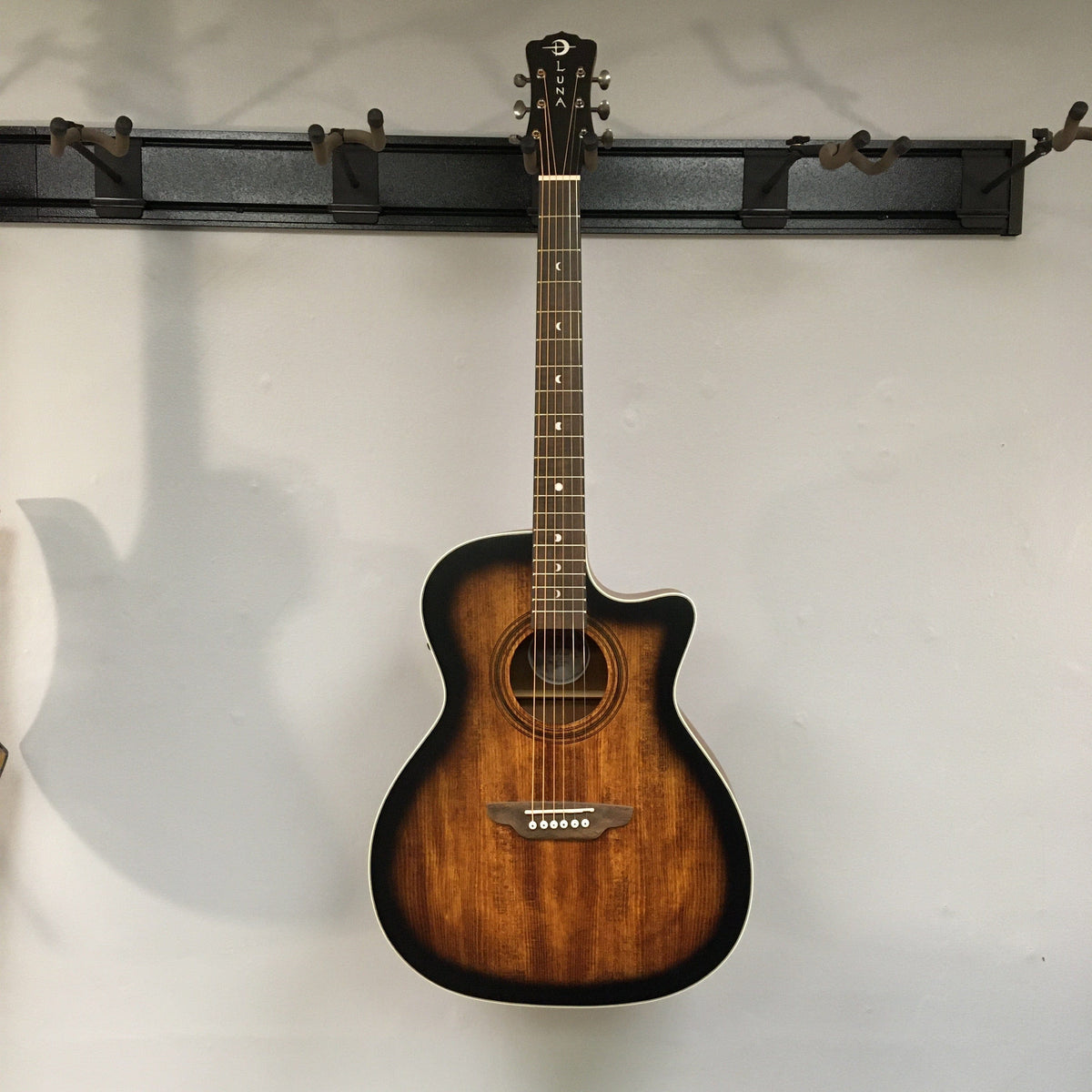 Luna Art Vintage Grand Auditorium Solid Top Cutaway A/E guitar mounted on a wall, showcasing its vintage brown burst finish and distinct rustic look.