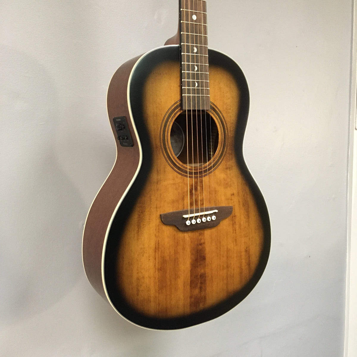 Luna Art Vintage Parlor Solid Top Distressed Vintage Brownburst guitar displayed on a wall, highlighting its detailed craftsmanship and rustic finish.