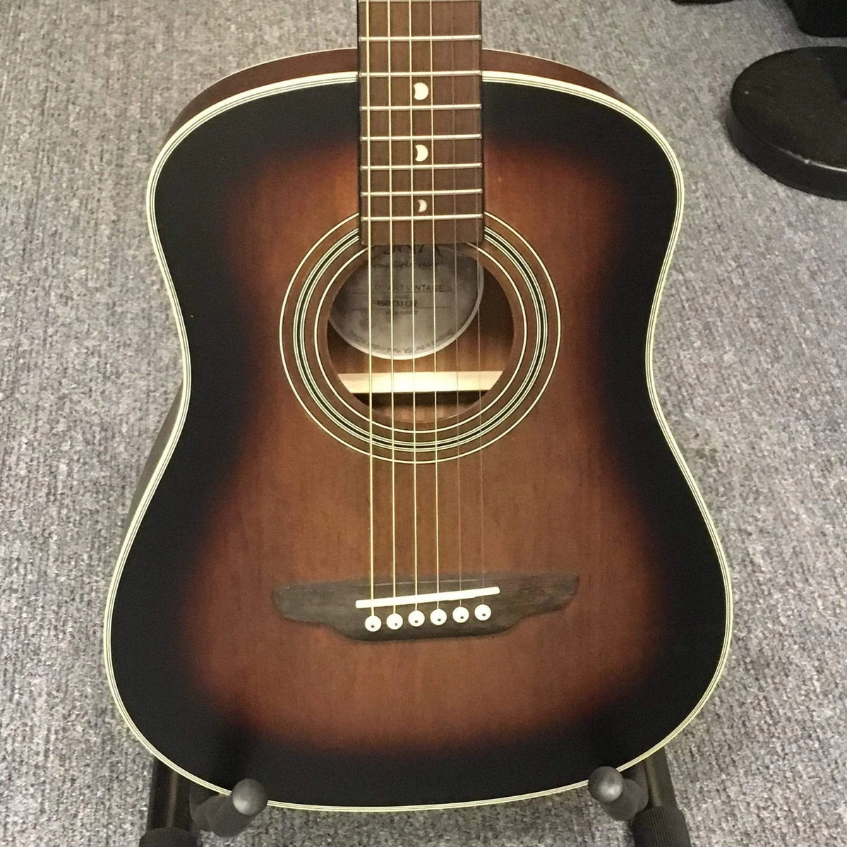 Luna Safari Artist Vintage Travel Guitar on a stand, showcasing its mahogany body, spruce top, and pearl moon phase inlays.