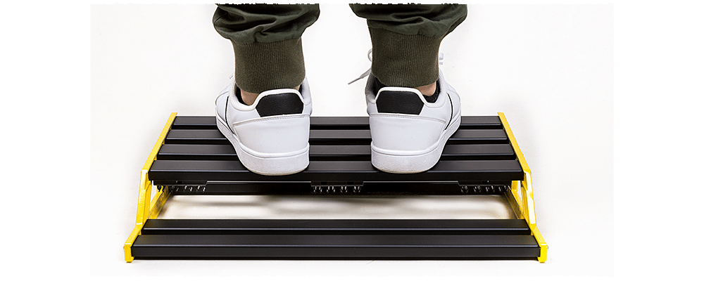 Person's feet in white shoes on NUX Bumblebee-M Pedal Board, highlighting customizable platform assembly for efficient pedal arrangement.