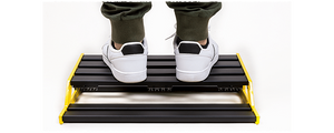 Person's feet in white shoes on NUX Bumblebee-M Pedal Board, highlighting customizable platform assembly for efficient pedal arrangement.
