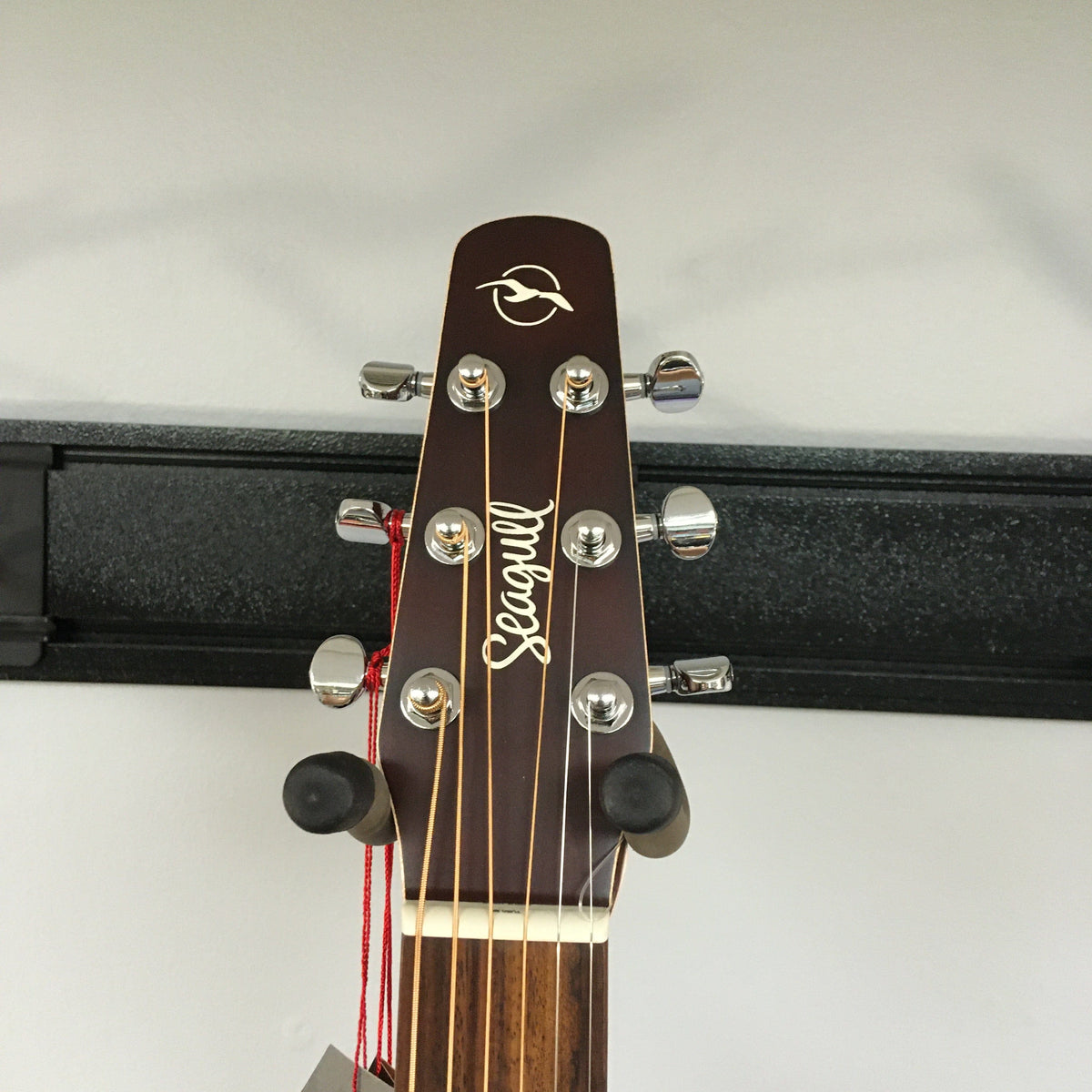 Close-up of the Seagull Entourage Autumn Burst Acoustic Guitar headstock, showing tuning pegs, brand logo, and neck against a light wall and black rack.