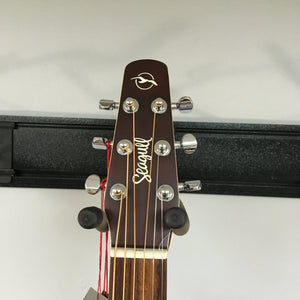 Close-up of the Seagull Entourage Autumn Burst Acoustic Guitar headstock, showing tuning pegs, brand logo, and neck against a light wall and black rack.