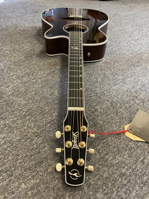 A Seagull Artist Mosaic CH CW Acoustic-Electric Guitar - Bourbon Burst (with TRIC Case) with a dark wood body and light trim rests on a gray carpet, headstock with brand name and tuning pegs closest to the camera, tag on one peg.